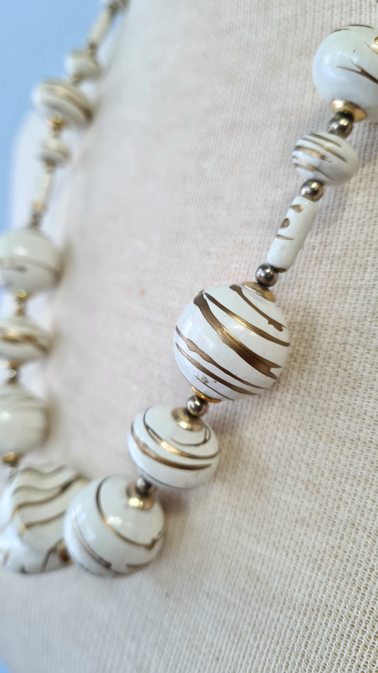 Valkoiset muovihelmet kullan sävyisillä raidoilla kaulakoru